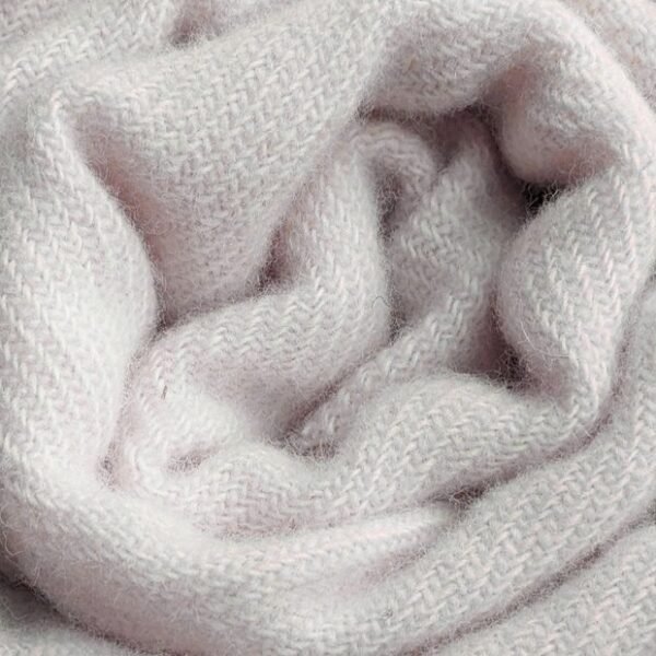 A close-up of a soft, pale pink knit scarf loosely twisted into folds, showing its textured woolen fabric.