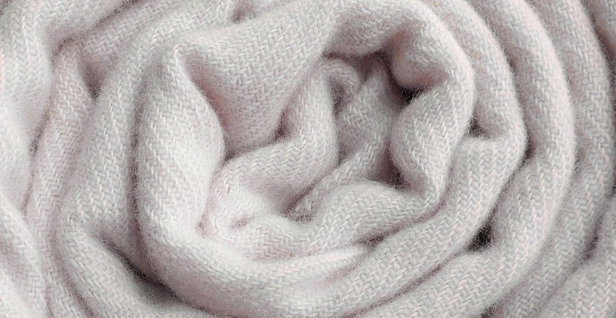 A close-up of a soft, pale pink knit scarf loosely twisted into folds, showing its textured woolen fabric.