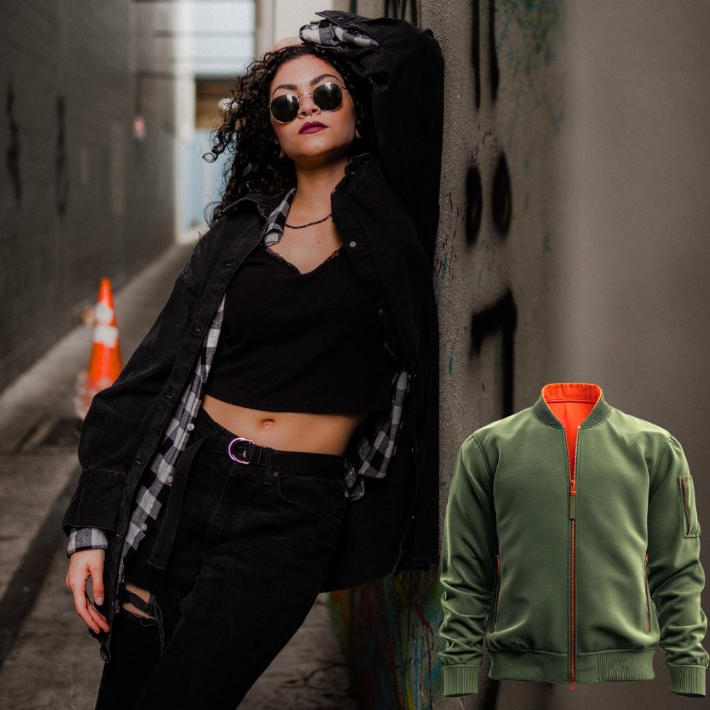 A stylish young woman leans against a graffiti-covered alley wall, wearing a black crop top, black jeans with a belt, a plaid shirt layered under a black jacket, round sunglasses, and dark lipstick. An orange traffic cone is visible in the background. A green bomber jacket with an orange lining appears as a separate image inset on the right.