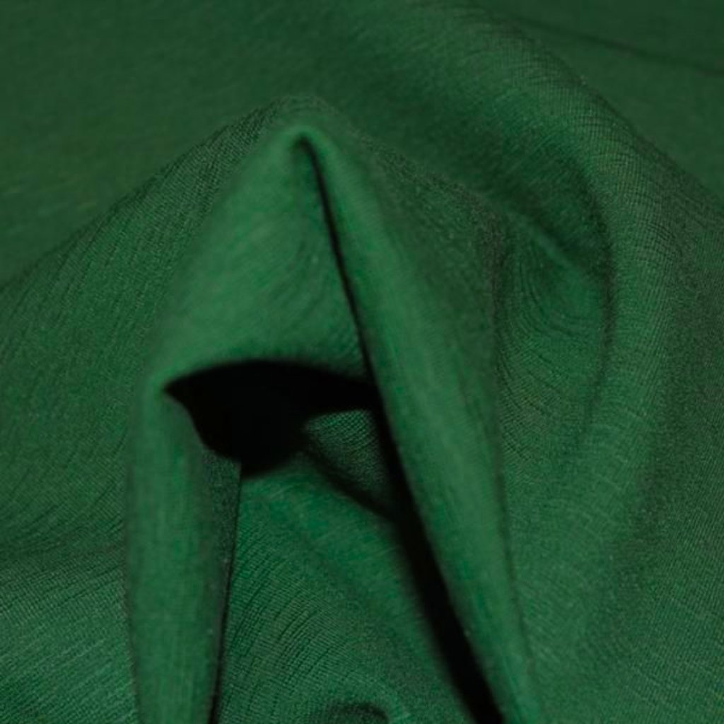 A close-up shot of dark green fabric with folds and a seam, creating a small pocket-like opening and shadows.