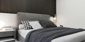 Best Cotton Blankets: Soft, Breathable, and Cozy Comfortable A modern bedroom with a gray upholstered bed, a dark wooden slat headboard, and matching gray nightstands. The bed has white sheets, several patterned pillows (black-and-white), and a dark gray blanket folded at the foot. A small gold desk lamp and a few decor items sit on the nightstands. Best Cotton Blankets
