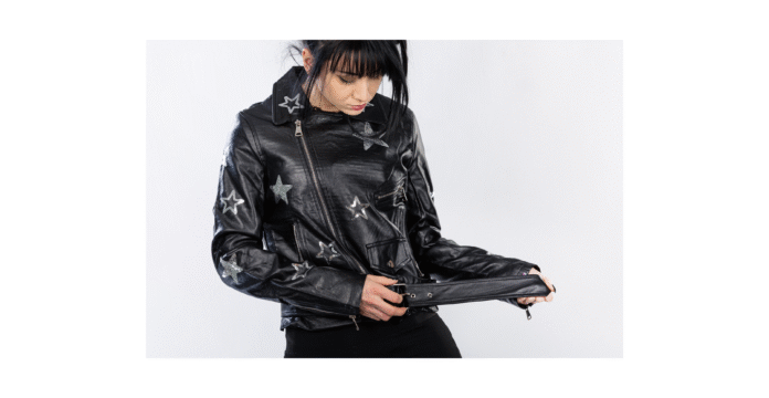 Close-up of a person wearing a black leather biker jacket adorned with silver star patches; the zipper is partially open and the person is pulling at the belt at the waist.