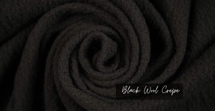 A close-up view of soft, black wool crepe fabric, showing its smooth, velvety texture and rolled fibers.