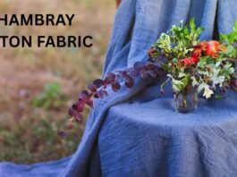 A person draped in blue chambray fabric sits outdoors with a vase of colorful flowers on their lap.