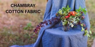 Chambray Cotton Fabric: Features, Uses, and Care Guide A person draped in blue chambray fabric sits outdoors with a vase of colorful flowers on their lap.