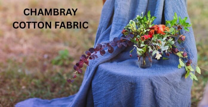 A person draped in blue chambray fabric sits outdoors with a vase of colorful flowers on their lap.