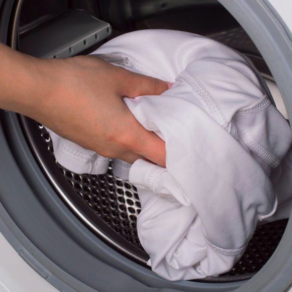 A hand places a white garment into a front-loading washing machine.