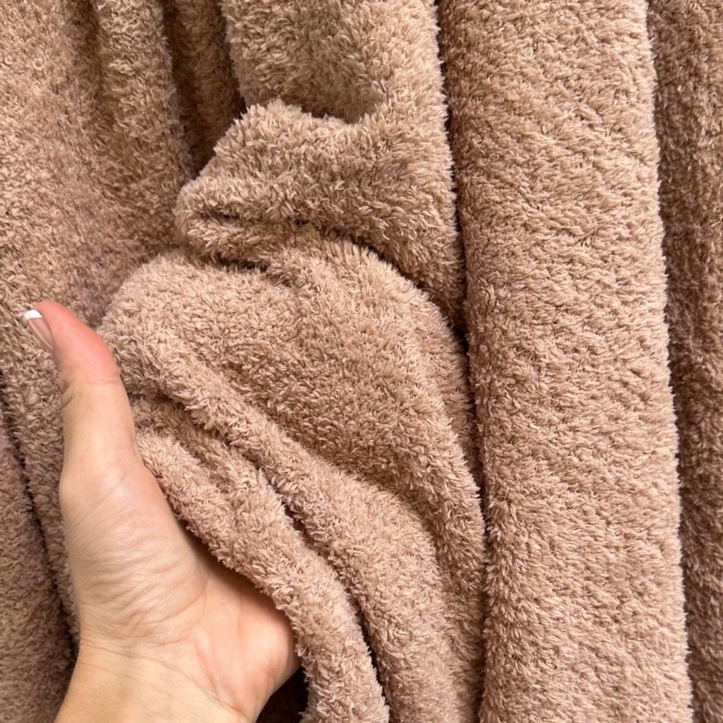 A close-up of a hand gripping soft, fluffy beige terry cloth fabric, showing the plush texture and folds.