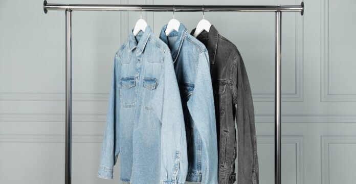 Three denim jackets hanging on a metal clothing rack.
