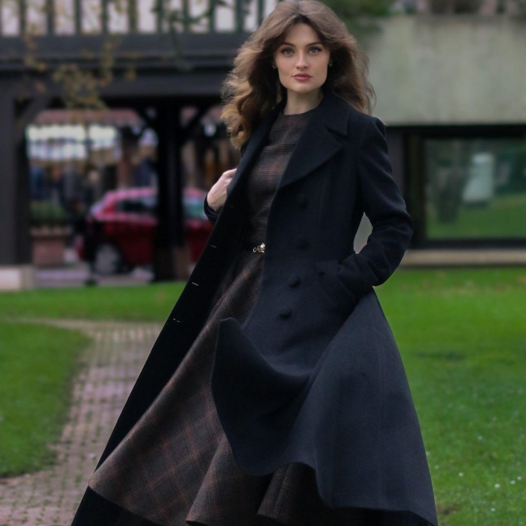 Woman in a dark navy long coat with a plaid dress underneath, walking outdoors on a path with green grass.