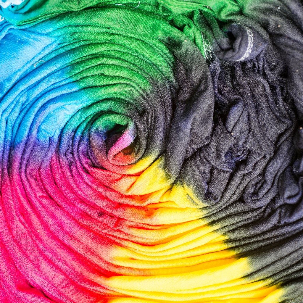 Coiled multicolored tie-dye fabric with a rainbow gradient transitioning from pink and red at the bottom to orange, yellow, green, blue, and black toward the top. Ease of Dyeing and Design