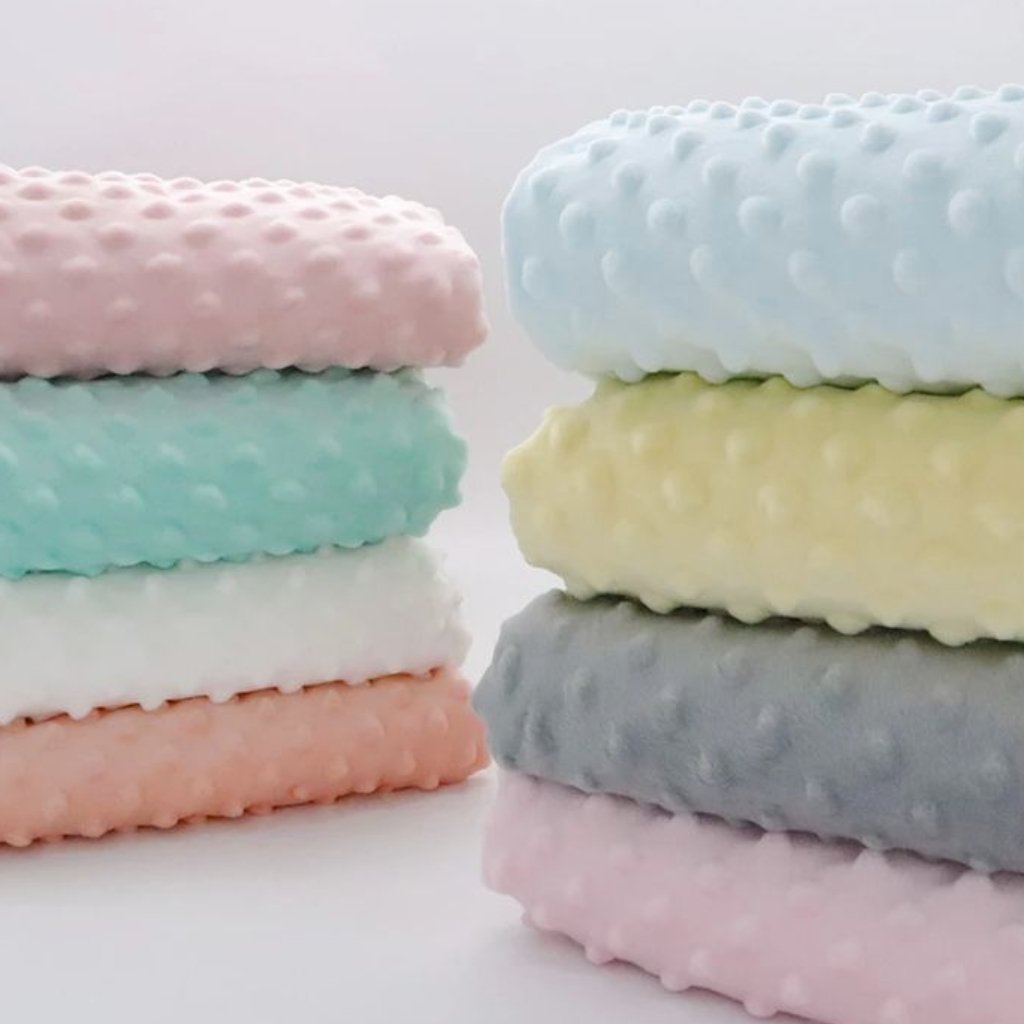 A stack of soft, pastel-colored towels with a dotted texture. The colors include pink, mint, white, peach, lavender, blue, and gray, arranged in two stacks.