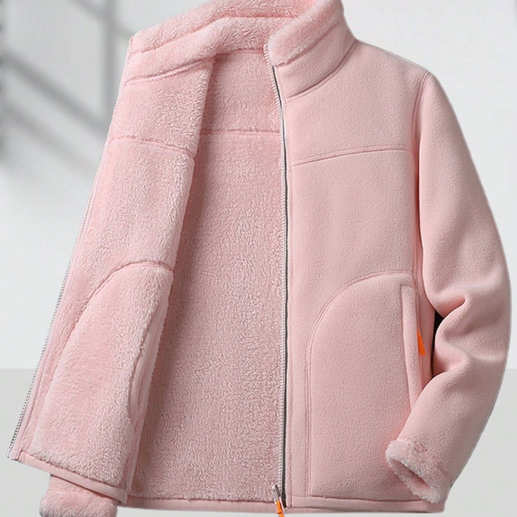 A soft pink shearling jacket with a half-zip front, featuring a two-tone texture—fuzzy shearling lining on the left panel and a smooth fabric on the right. It has a stand collar, zippered cuffs, and curved pocket seams.


