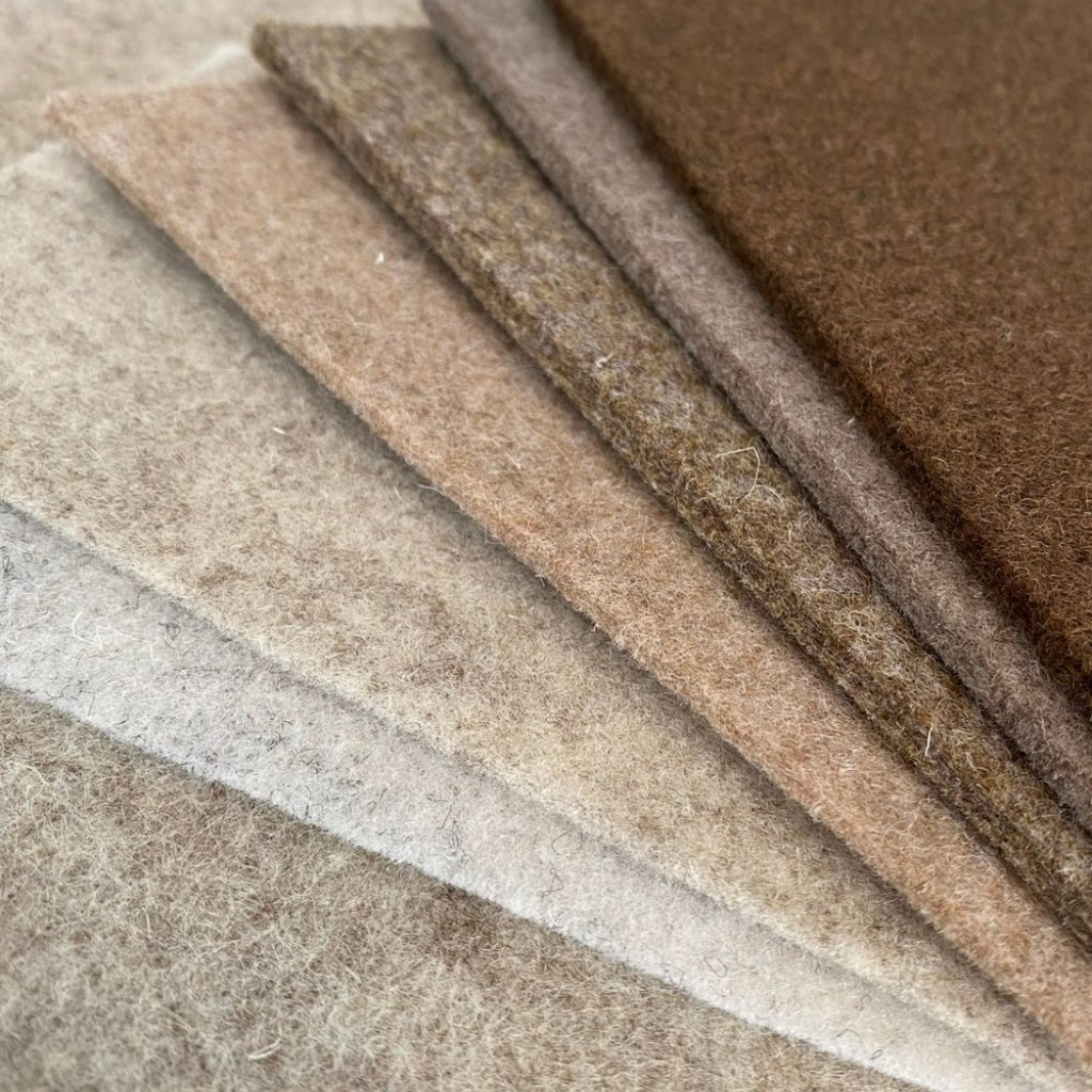 Felted Merino Fabric: Premium Softness for Cozy Elegance 8 A close-up view of several stacked felt sheets in neutral tones (beige, tan, light brown, and brown), showing the soft, fuzzy texture and layered edges.