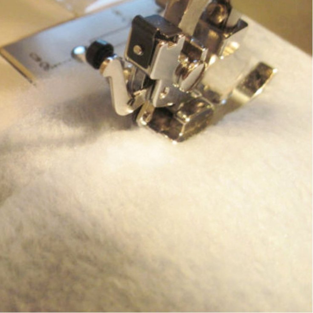 A close-up of a sewing machine presser foot and needle assembly resting on white fabric, with metallic components and a small black knob visible.