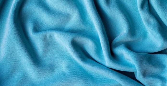 A close-up shot of smooth, bright blue fabric with soft folds and gentle shadows.
