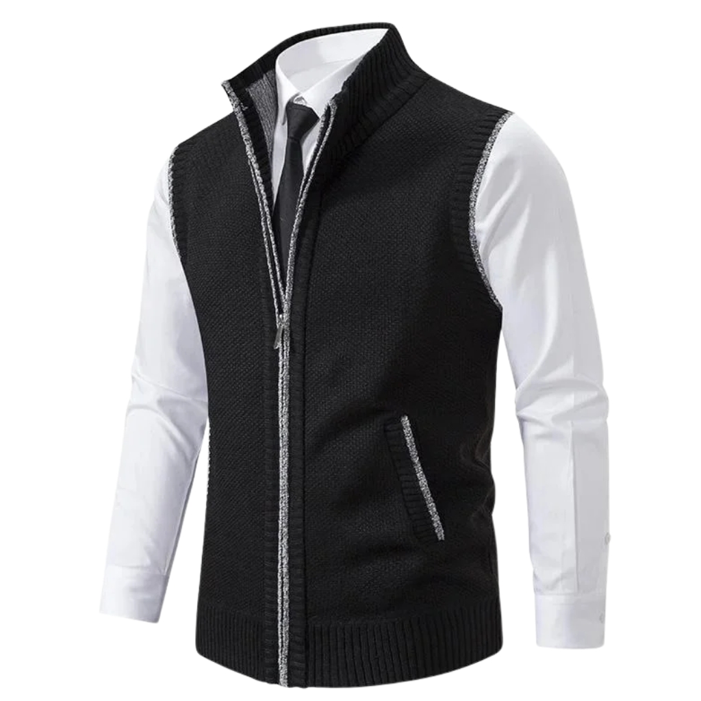 A black knitted zip-up vest worn over a white dress shirt and tie. It features a high ribbed collar, silver stitching along the zipper and pocket trim, and ribbed hem.