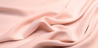 Is Rayon a Good Fabric? Everything You Need to Know. A soft, pale pink fabric draped in smooth folds, with a silky sheen.