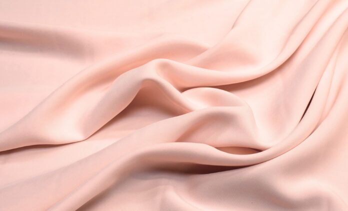 A soft, pale pink fabric draped in smooth folds, with a silky sheen.