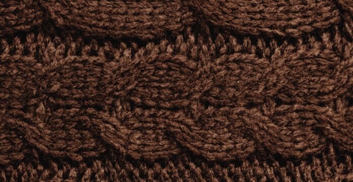 Close-up of dark brown knitted fabric with a cable stitch pattern. Jersey Knit