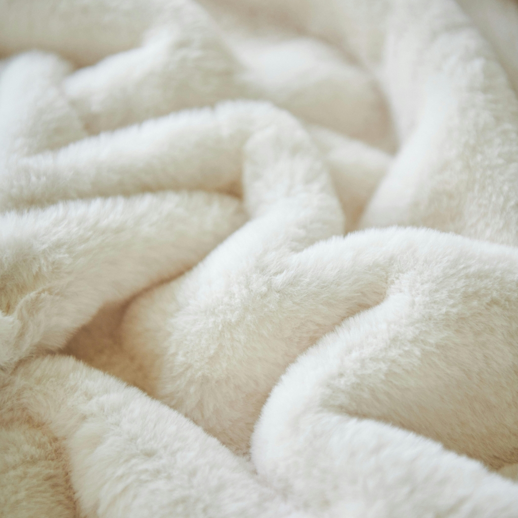 Close-up of fluffy, cream-colored fleece fabric with soft, plush texture and folds.