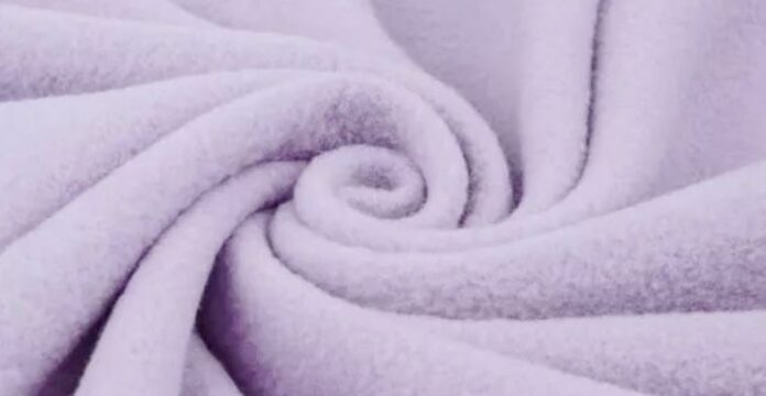 Close-up of soft, light purple Merino fleece fabric folded into gentle curves, showcasing its smooth, fluffy texture