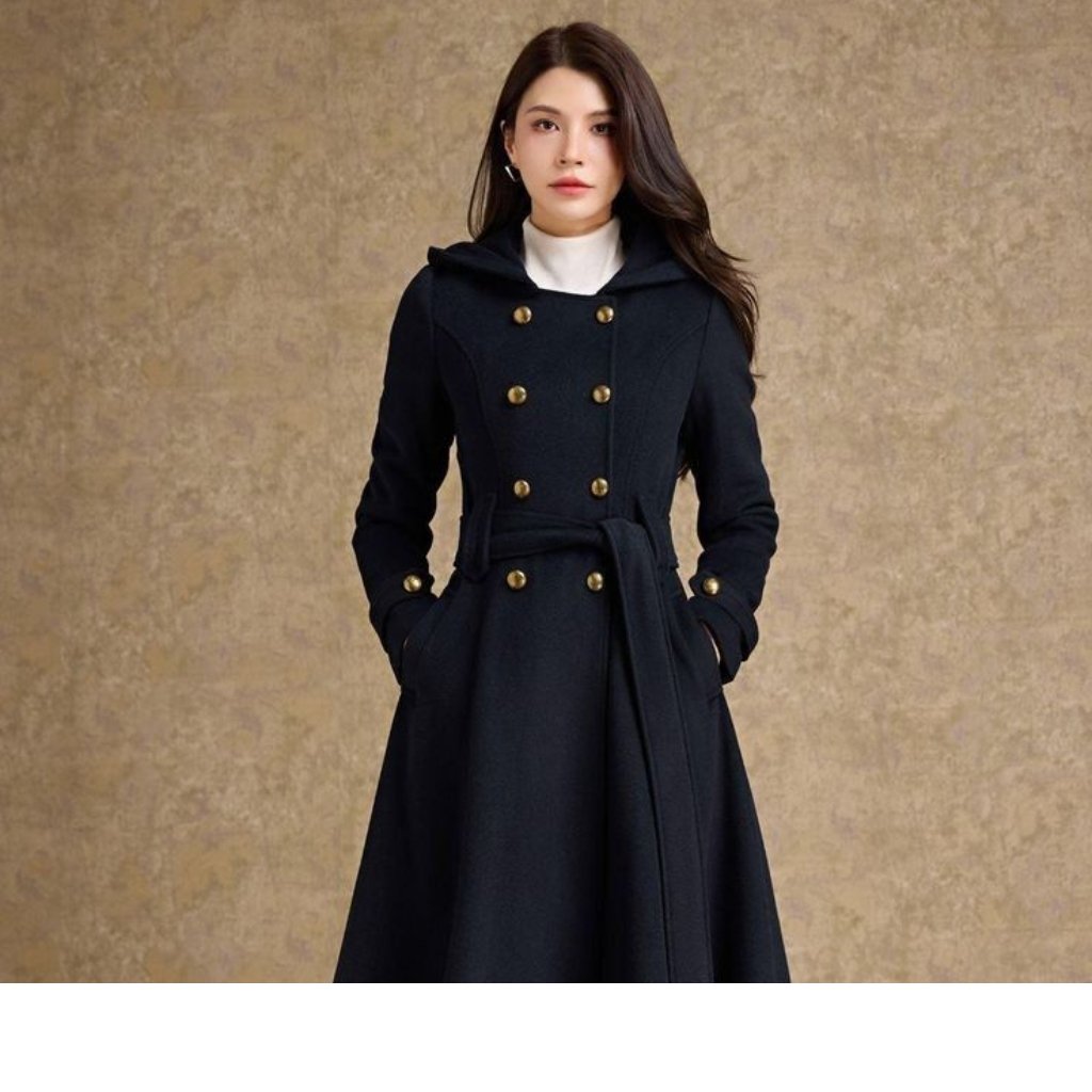 Woman wearing a black double-breasted long coat with gold buttons and a belt, standing against a beige textured background.