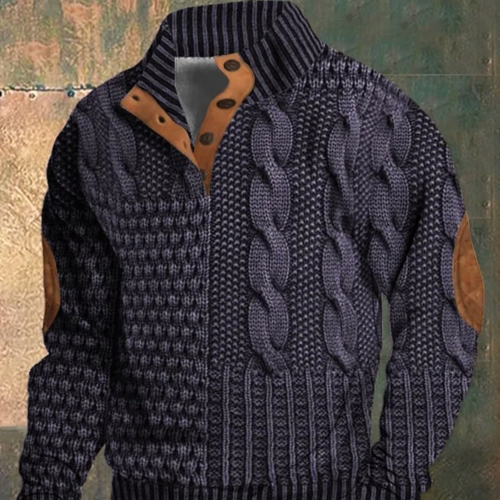 A dark blue cable-knit sweater with intricate braided patterns, brown suede elbow patches and a striped collar, displayed on a mannequin against a textured background. Mons Royale – Bold Designs, Natural Performance
