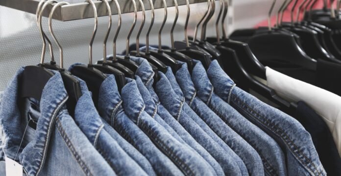A row of denim jackets hanging on black hangers along a clothing rack.