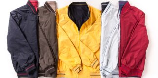 Performance Track Jacket: Top Features Athletes Should Know. A row of six lightweight jackets in different colors (navy, brown, mustard yellow, light gray, and red) laid flat side by side with their zippers and cuffs visible. Performance Track Jacket