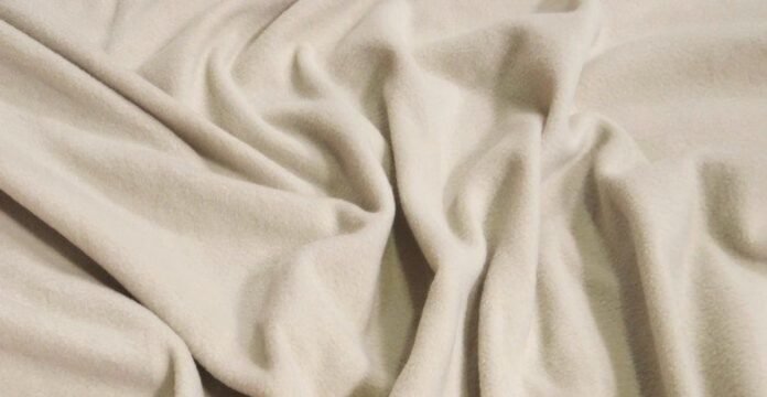 Close-up of soft, cream-colored fabric with gentle folds and drapes. Polar Fleece Fabric
