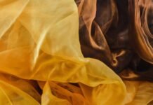 Silk Organza Fabric: The Perfect Choice for Elegant Fashion A close-up view of sheer silk organza fabric in warm amber and honey tones, with delicate, translucent folds and soft light.