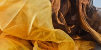 Silk Organza Fabric: The Perfect Choice for Elegant Fashion A close-up view of sheer silk organza fabric in warm amber and honey tones, with delicate, translucent folds and soft light.