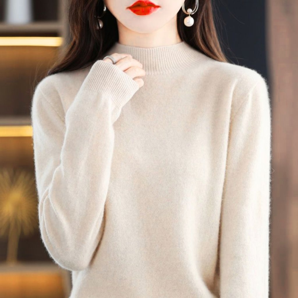 A close-up of a person wearing a soft, cream-colored knit sweater with a ribbed crew neck. The person has red lipstick and is accessorized with dangling pearl earrings; one hand rests near the collar.
