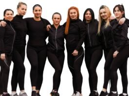 Group of nine women standing close together, wearing black athletic outfits, against a white background. Streetwear Track Jacket