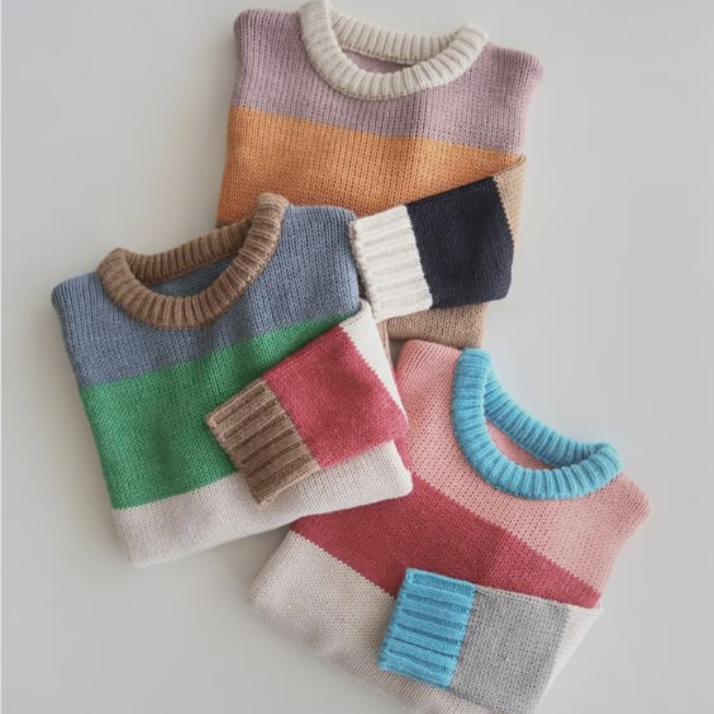 Three folded color-block knitted sweaters with contrasting ribbed collars and cuffs in pastel tones, arranged in a fan-like display.
