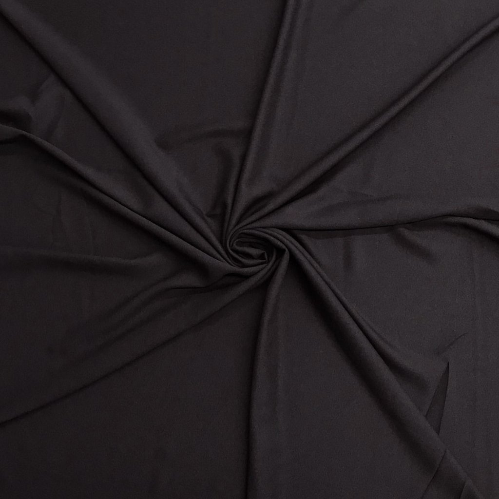A close-up view of smooth black fabric gathered and twisted at the center, creating soft folds and a subtle spiral pattern.