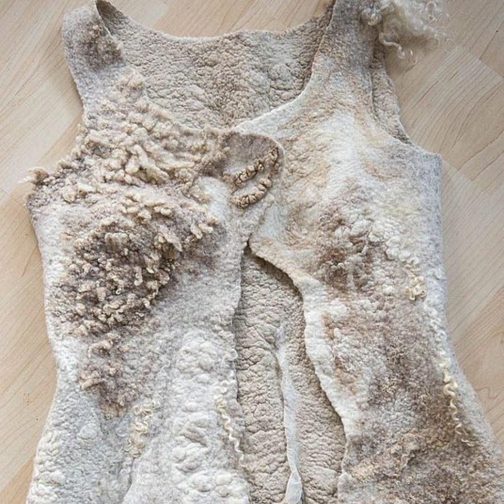 Felted Merino Fabric: Premium Softness for Cozy Elegance 12 A textured, weathered sleeveless garment laid flat on a wooden surface. The fabric appears crusty and fossil-like with irregular ruffled edges and raised, bumpy patterns across the chest and sides.