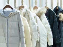 A row of insulated winter jackets hanging on wooden hangers against a light background.