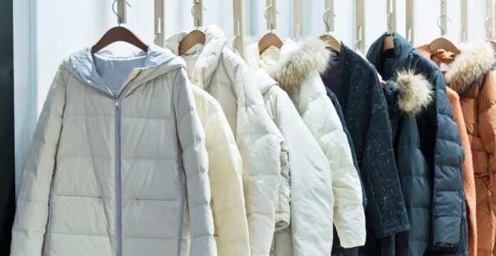 A row of insulated winter jackets hanging on wooden hangers against a light background.