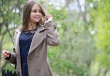 Topcoat Jackets Stylish Outerwear for a Sharp Seasonal Look A young woman wearing a beige trench coat over a dark blue dress walks through a green, leafy park, smiling and looking to the side while adjusting her hair; she holds an umbrella in one hand. Topcoat Jackets