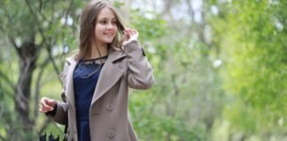 Topcoat Jackets Stylish Outerwear for a Sharp Seasonal Look A young woman wearing a beige trench coat over a dark blue dress walks through a green, leafy park, smiling and looking to the side while adjusting her hair; she holds an umbrella in one hand. Topcoat Jackets