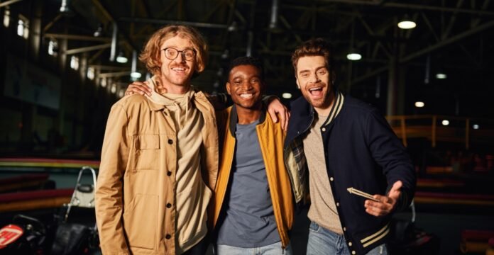 Three smiling young men standing together indoors at a recreation venue, arms around each other. Track Jackets