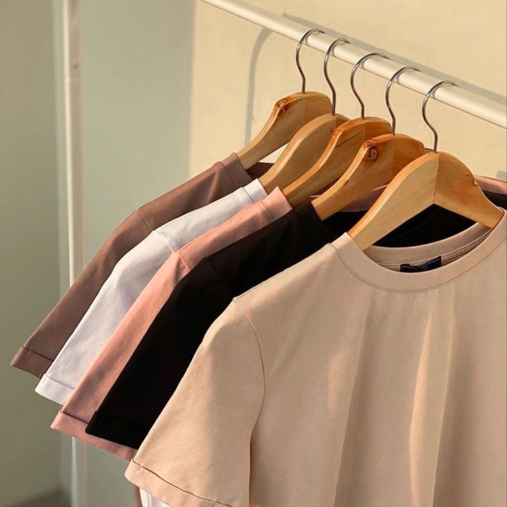 A row of pastel and neutral-colored T-shirts on wooden hangers hanging on a metal rack.