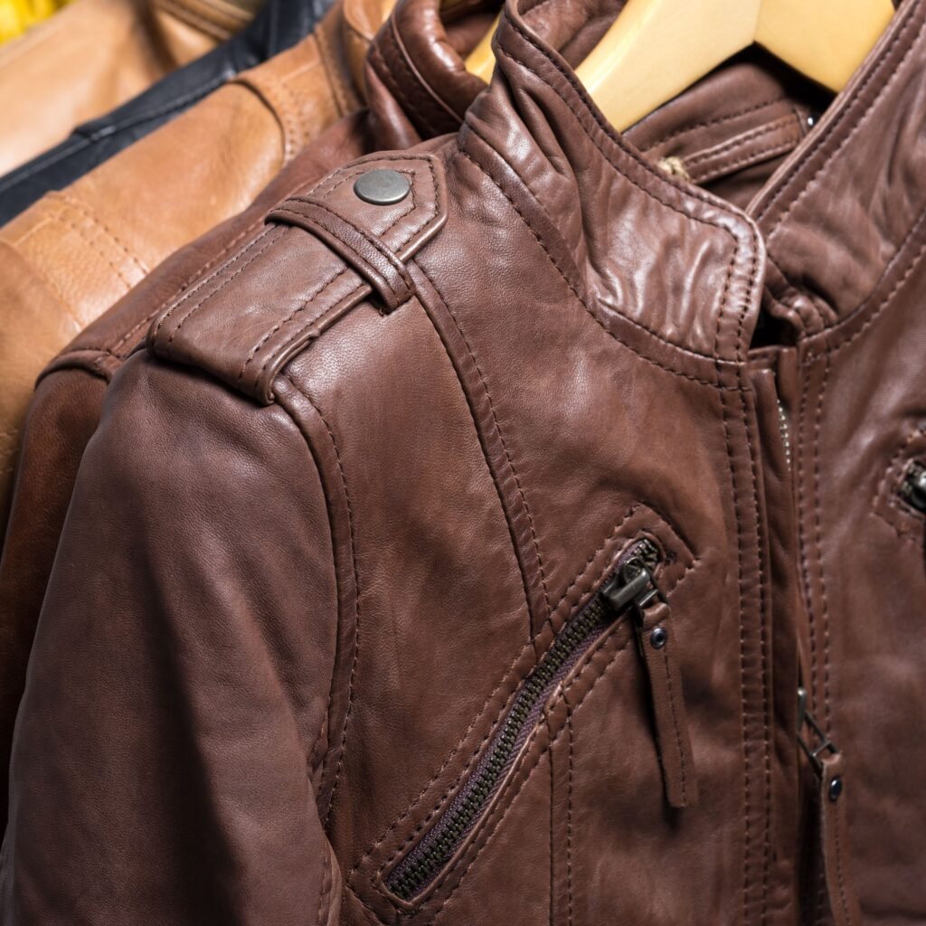 Close-up of a brown field leather jacket with a zipper pocket, shoulder strap detail, and stitched seams.
