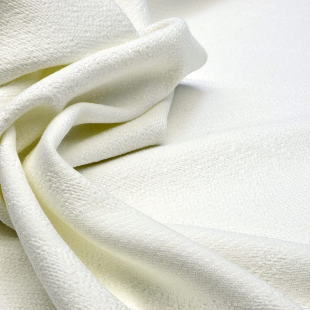 A close-up of soft, white cotton fabric with gentle folds and a textured weave.