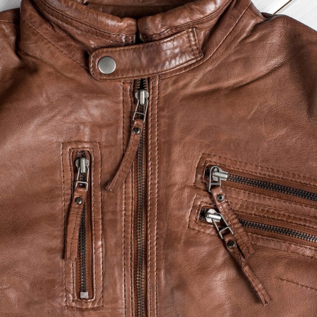 Modern Field Leather Jacket: Fresh Urban Look with Function 8 A close-up shot of a brown leather jacket featuring multiple zippers and a snap-fastened collar strap, highlighting the jacket’s rugged texture and hardware.