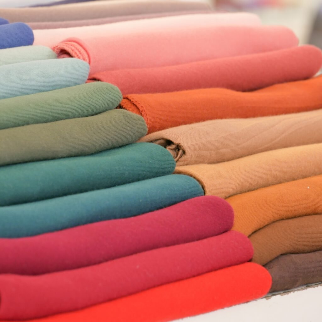 A neatly stacked pile of folded fabrics in a rainbow of colors, including blues, greens, pinks, oranges, and browns, with soft textures.