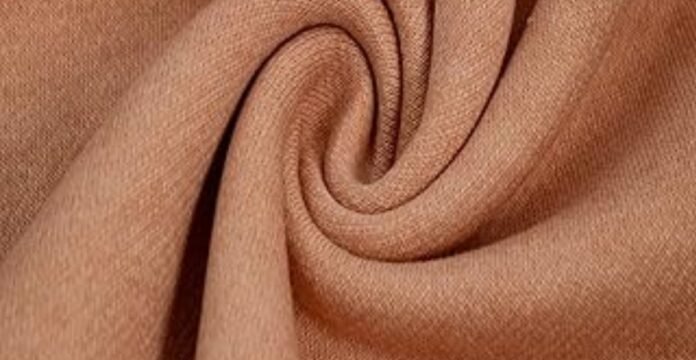 A close-up view of a soft, tan-colored polyester fabric twisted into a swirl, often used to illustrate questions like does polyester make you sweat due to its texture and weave.what is brushed cotton fabricwhat is brushed cotton fabric