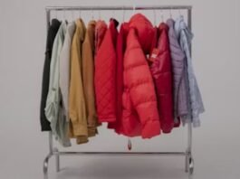 A clothing rack filled with various winter jackets in different colors, including red puffer jackets, beige coats, and pastel outerwear, arranged neatly against a plain background.Puffer Jackets